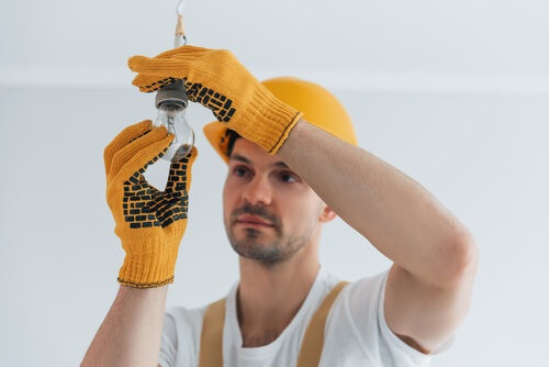 Handyman in yellow uniform changing light bulb. House renovation conception
