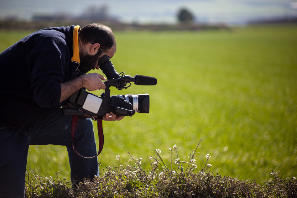 a cameraman with a professional camcorder in a green idyllic field